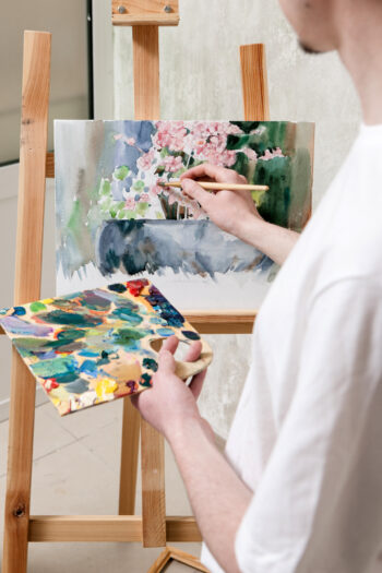 A painter painting a piece of art on a wooden easel. 